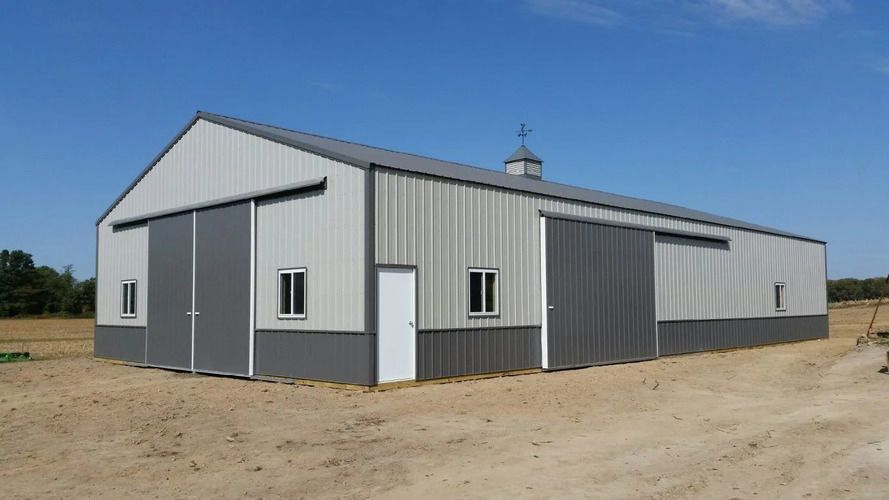 Gray and white metal barn under a clear blue sky, with sliding doors and a small cupola.