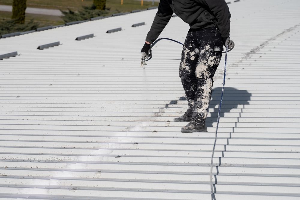 Person sprays white paint on a corrugated metal roof.