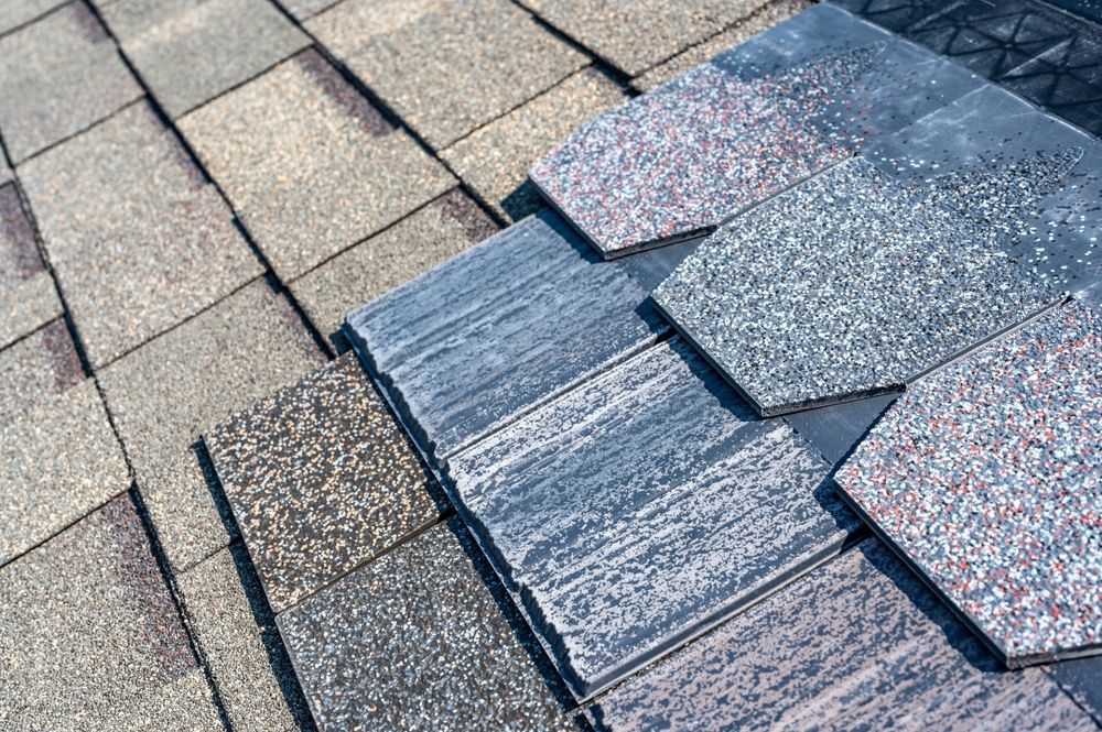 Close-up of overlapping asphalt roof shingles in shades of gray, brown, and black.