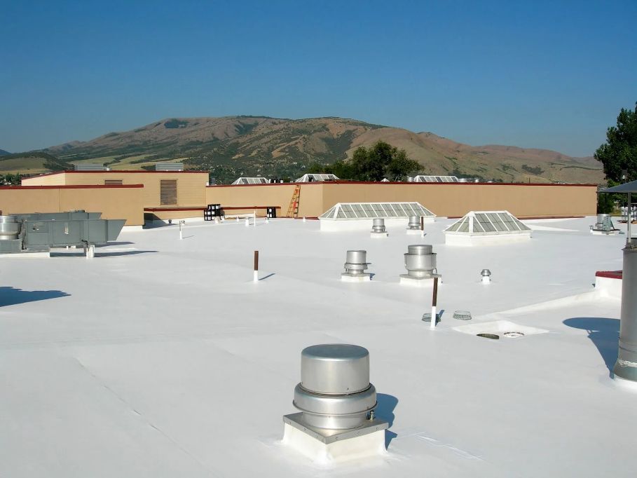 White flat roof with vents and a building, mountain in the background under blue sky.