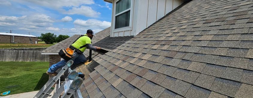 A roofer wearing safety gear working on a shingled roof under a blue sky.