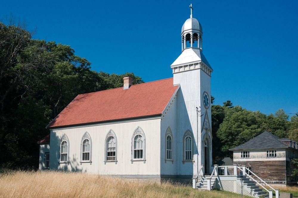 White church with red roof and silver steeple, set in a field with trees under a blue sky.
