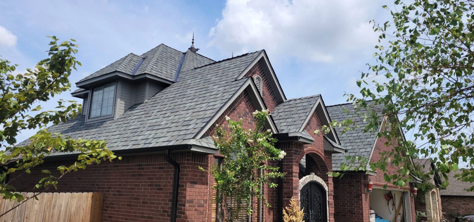Brick house with gray roof, windows, and trees in front of a blue sky.