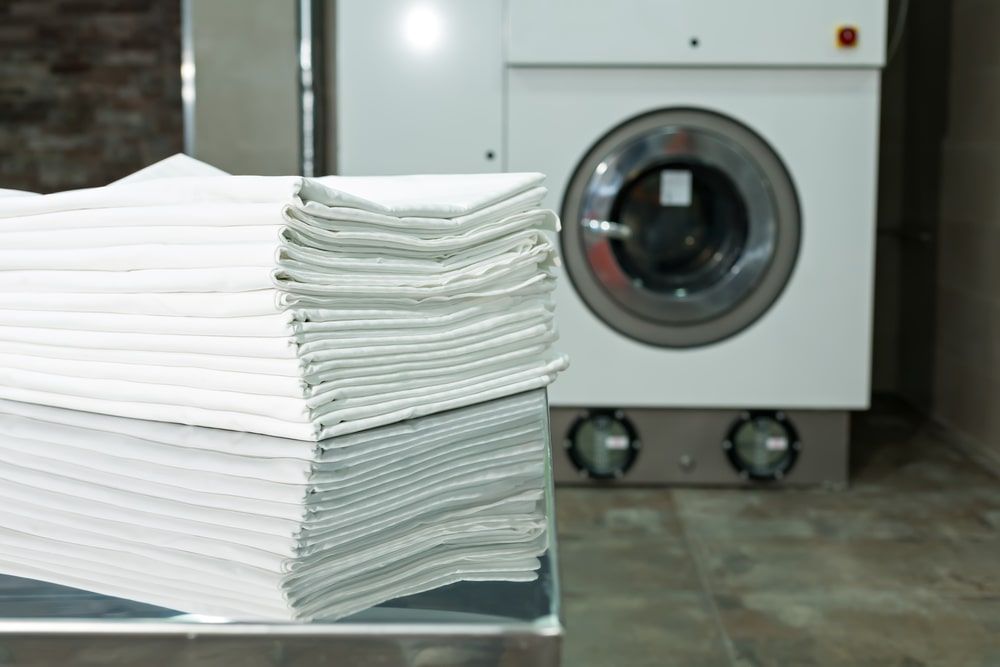 A Stack Of White Towels Sits Next To A Washing Machine — WashFold Laundromat In  Allenstown, QLD