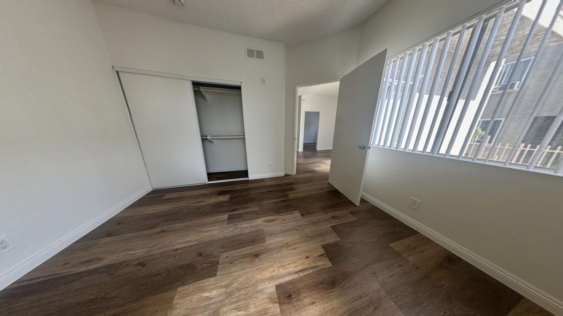 Empty room with wood floors, closet, and a window with blinds.