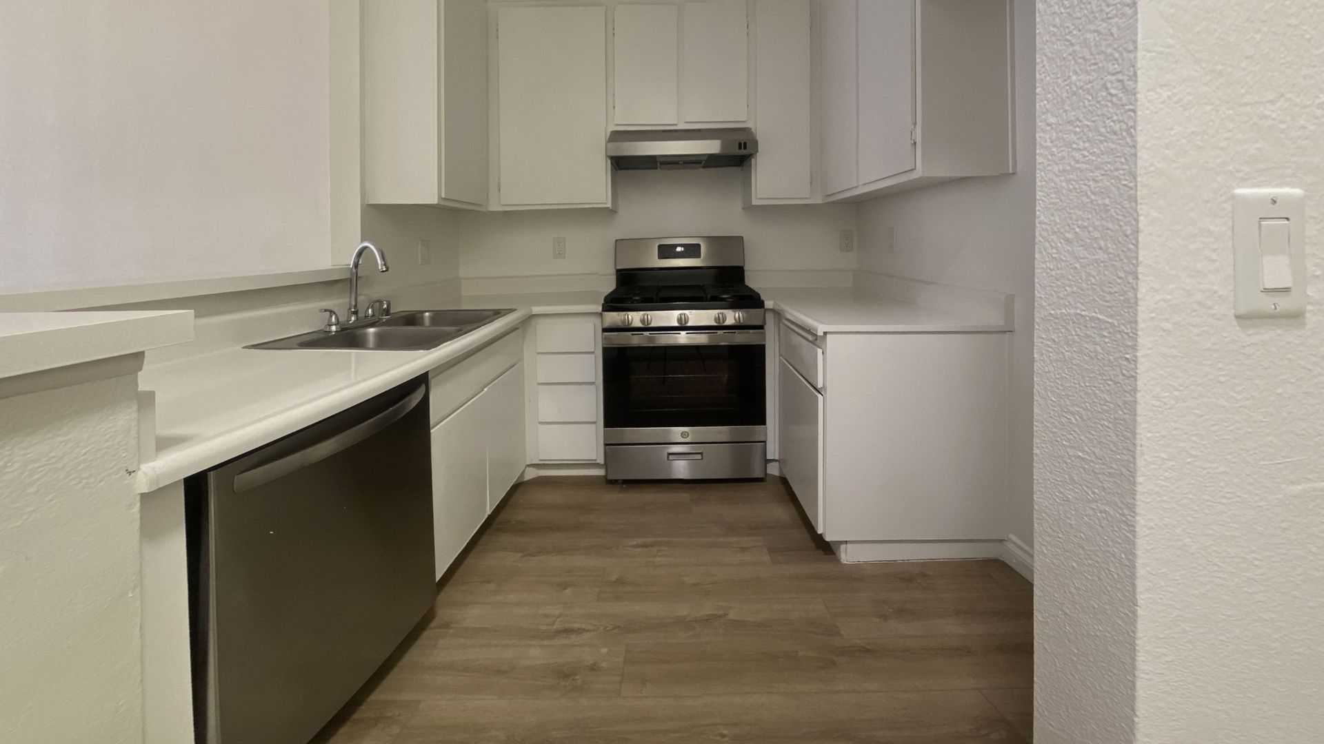 White kitchen with stainless steel appliances: oven, range hood, and dishwasher. Cabinets and countertops.