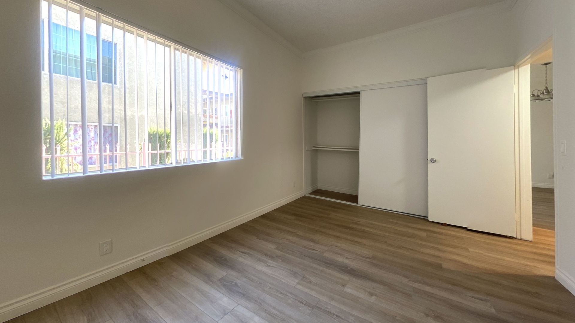 Empty bedroom with wood-look flooring, a window with blinds, closet, and a closed door.