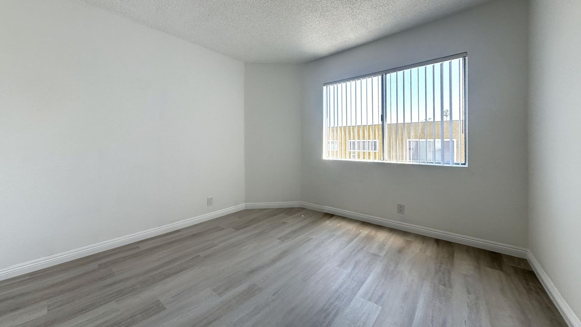 Empty room with white walls, window with blinds, and wood-look flooring.
