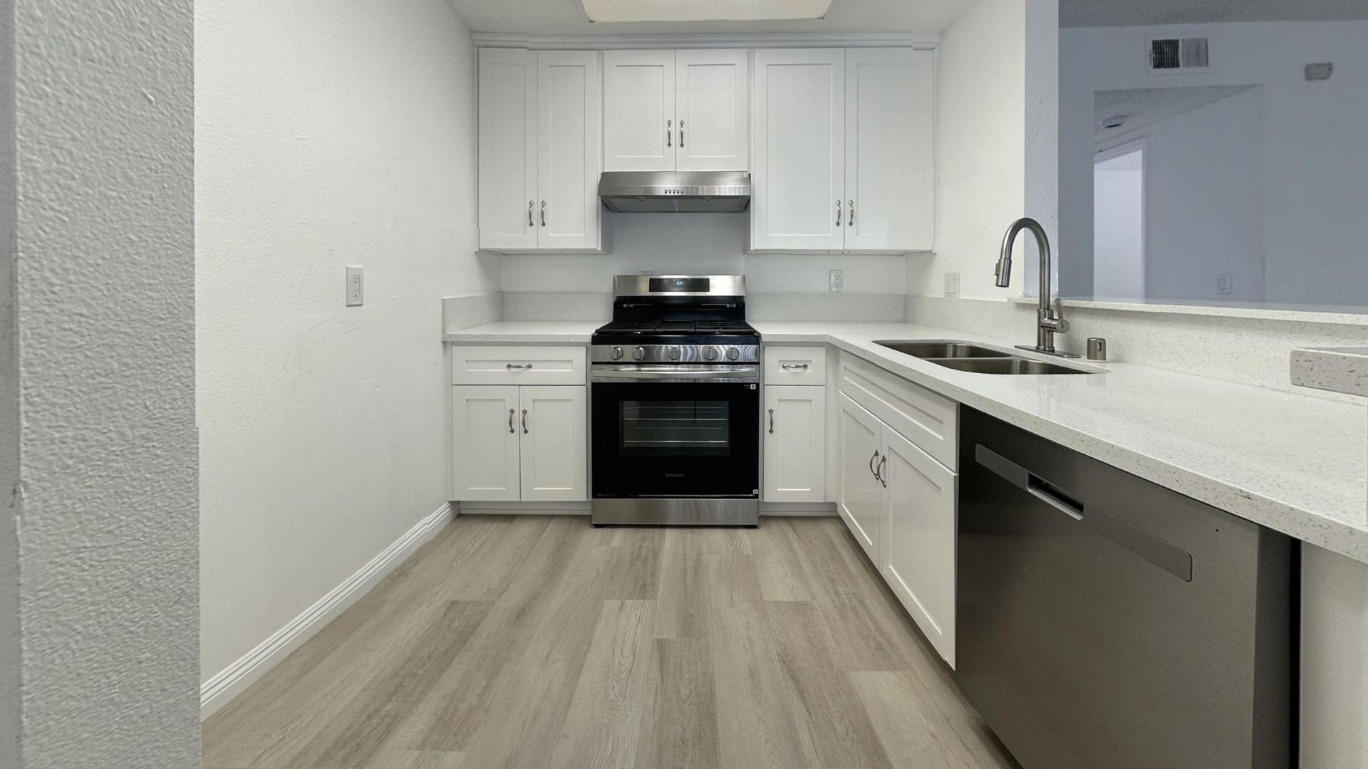 White kitchen with stainless steel appliances, white cabinets, light gray flooring, and countertop.
