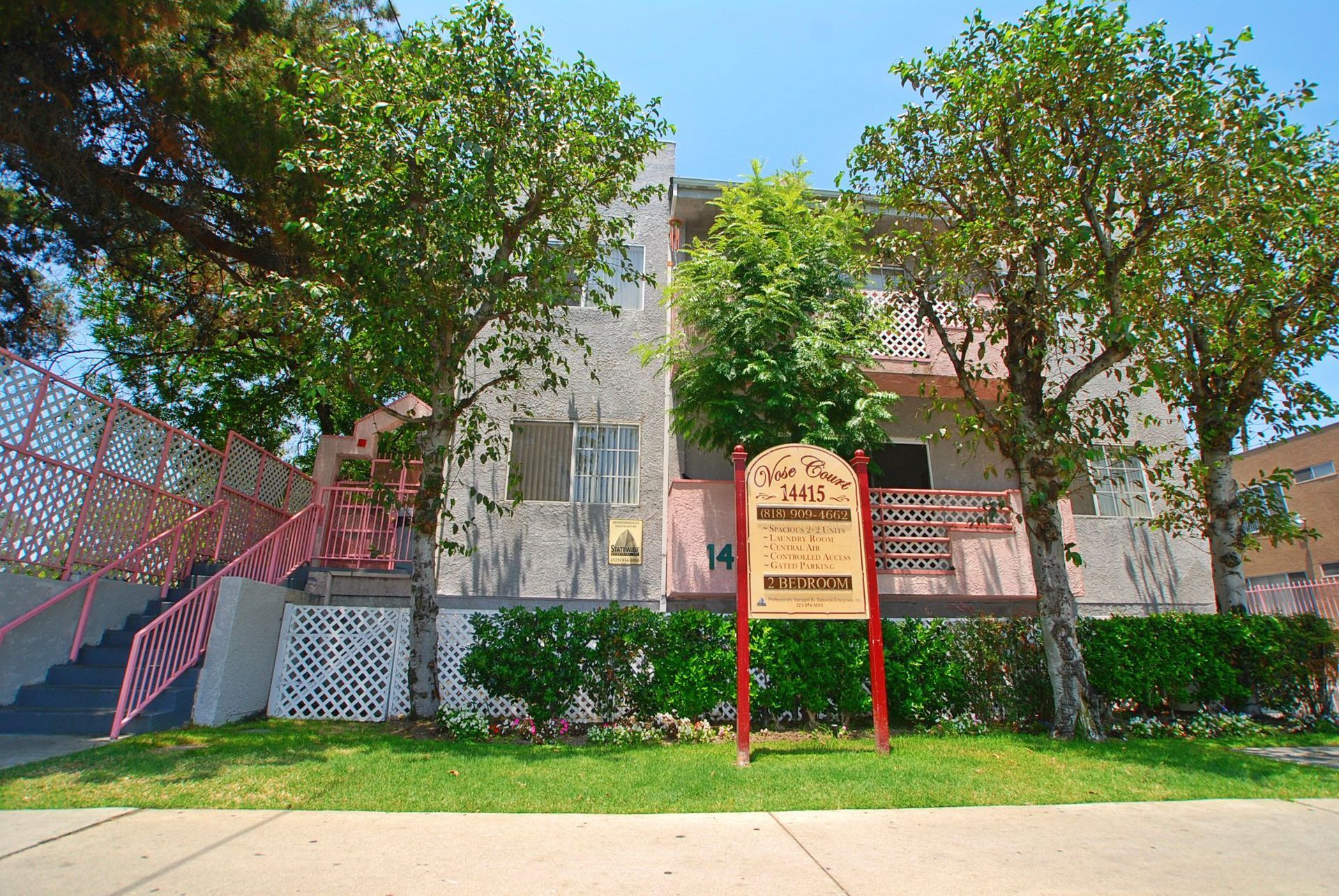 Apartment building, beige exterior, pink trim, sign in front, trees.