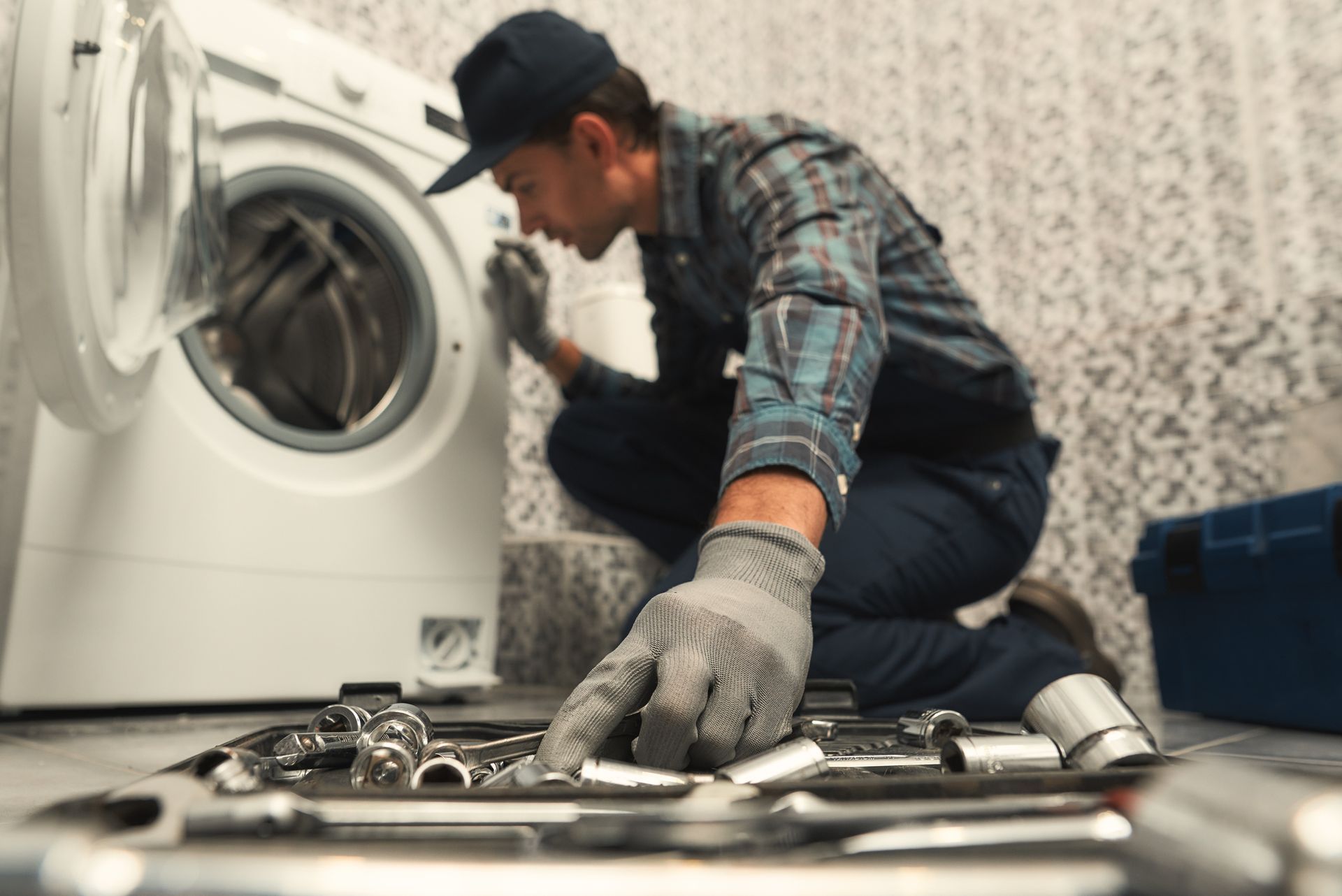 Person examining a washing machine, selecting a tool from a tray. 