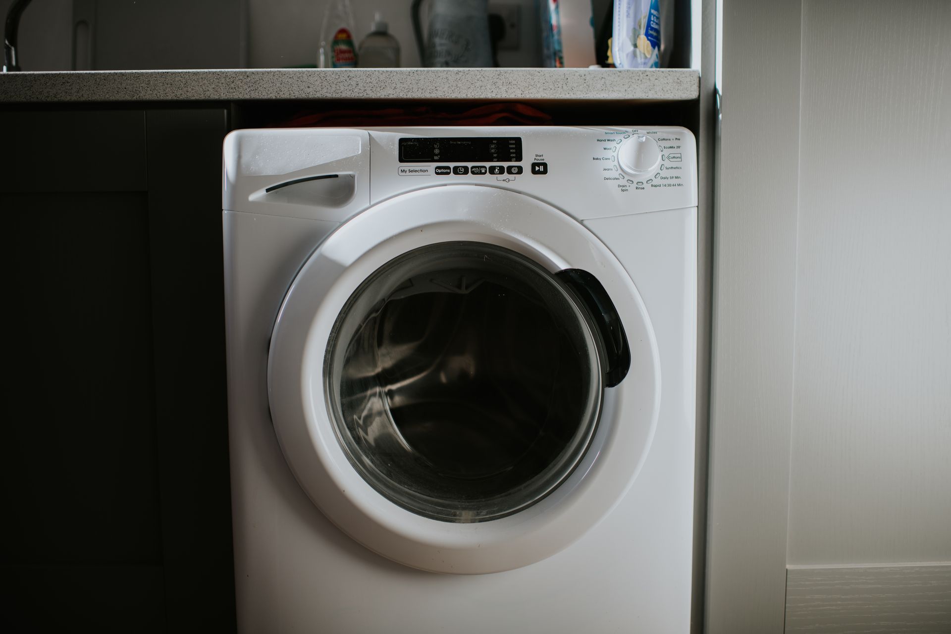 White washing machine, partially open, against a dark cabinet and light gray wall.