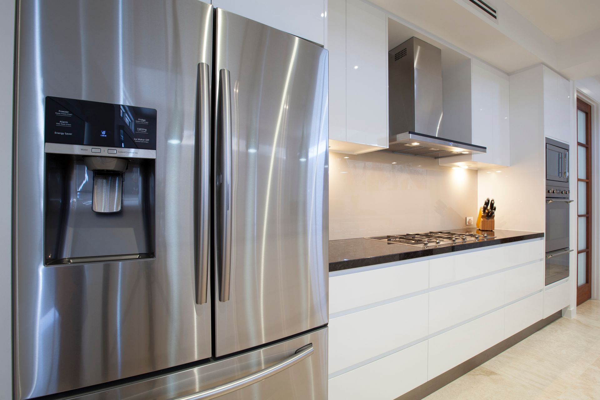 Stainless steel refrigerator and white modern kitchen with stovetop.