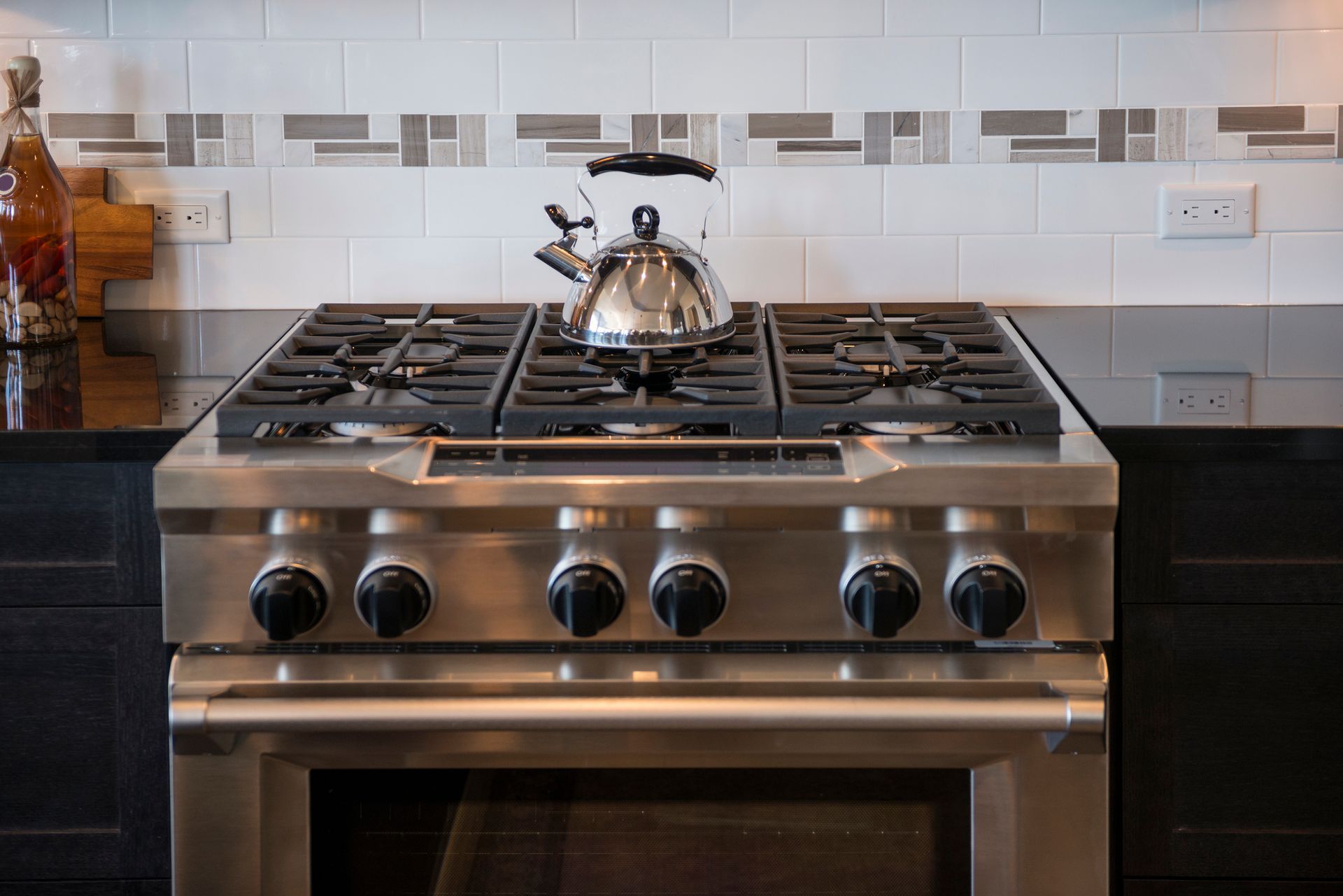 Stainless steel stove with a kettle on top; white tile backsplash.
