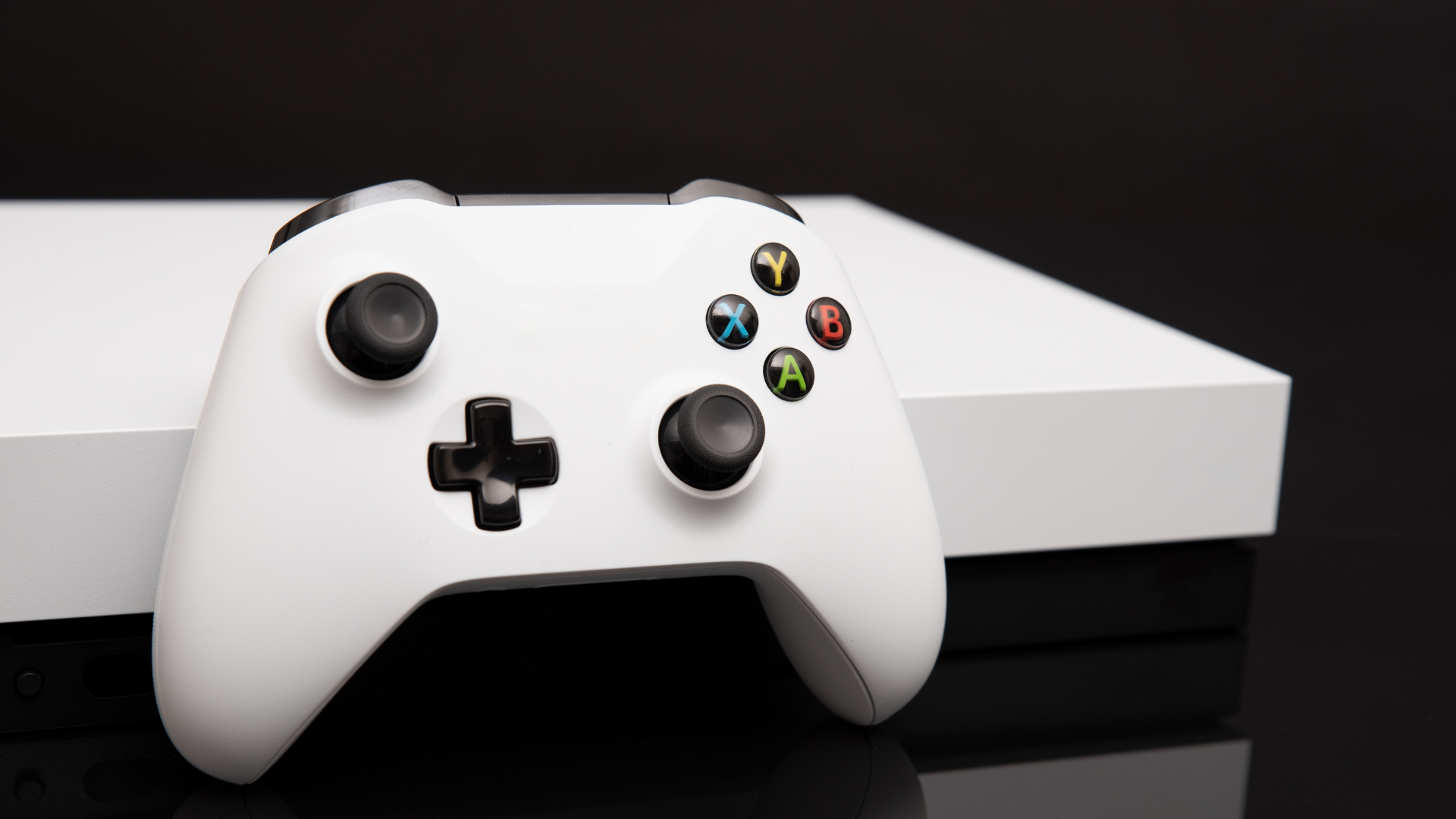 White Xbox controller on top of a white Xbox console against a black background.