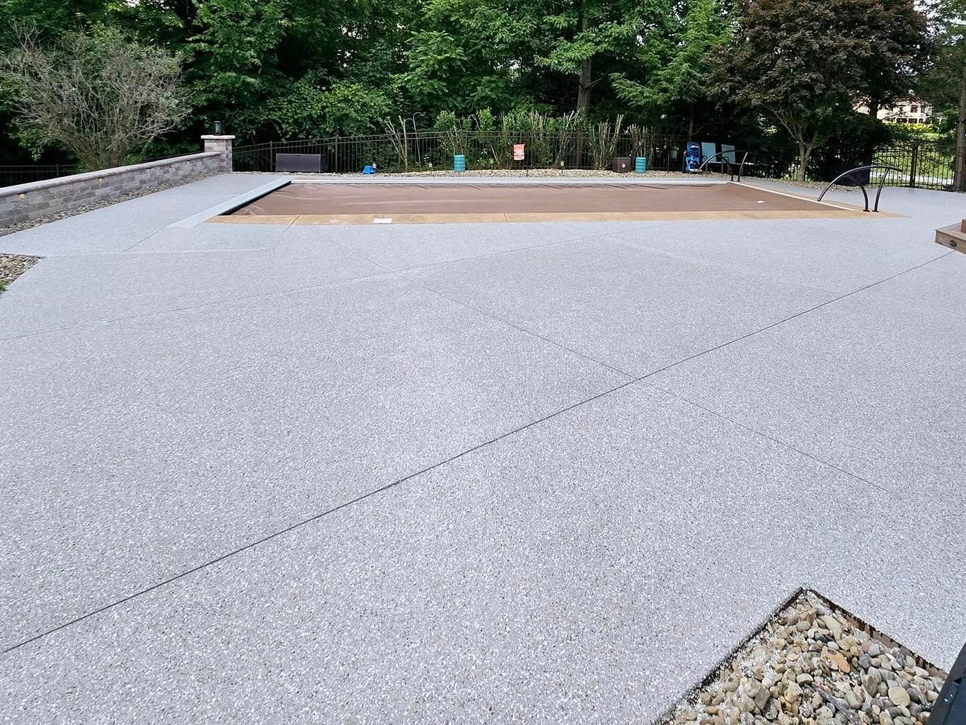A concrete driveway with a swimming pool in the background.