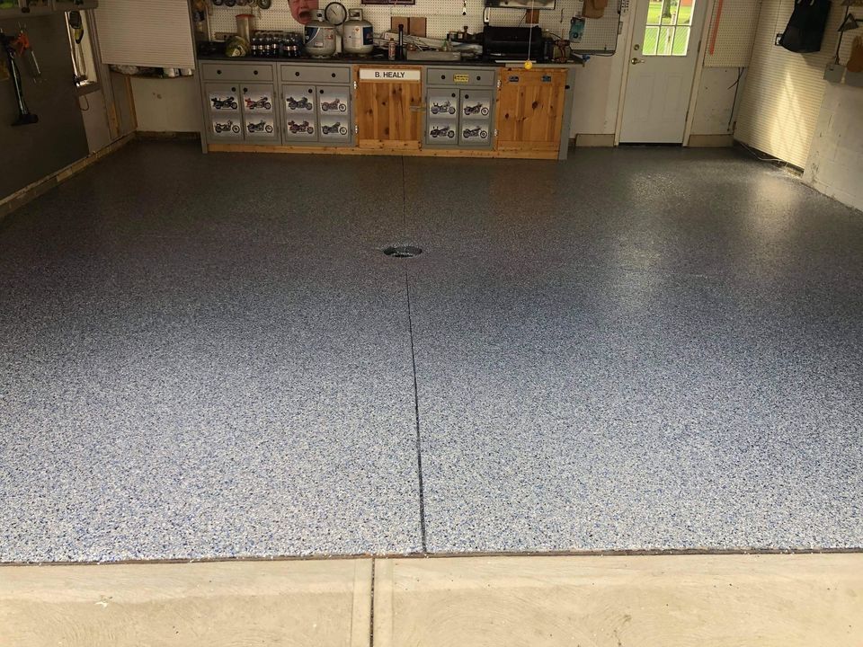 A garage with a gray floor and a kitchen in the background.