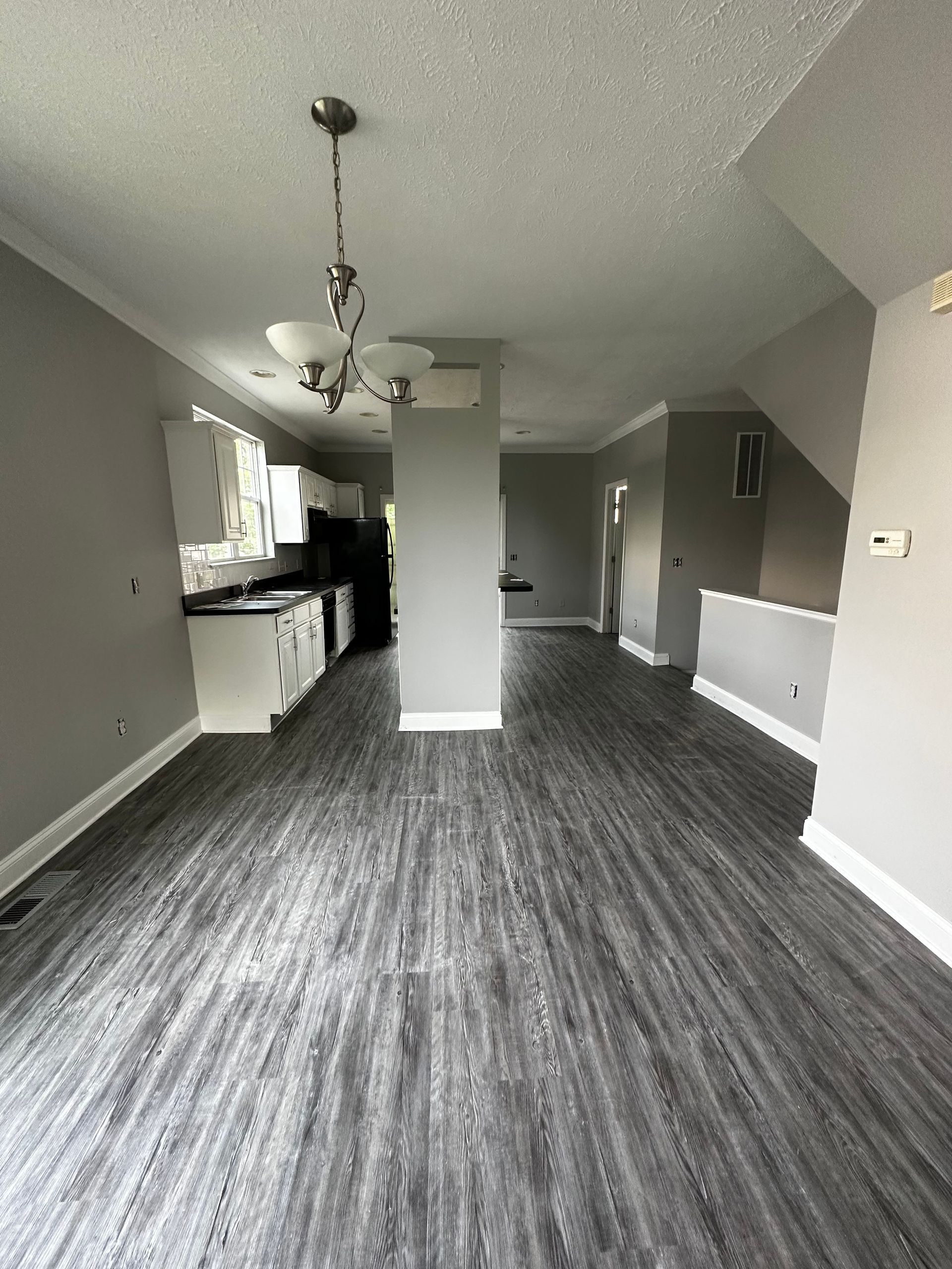 A large empty room with a wooden floor and a chandelier hanging from the ceiling.