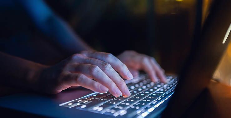 a person is typing on a laptop keyboard at night .