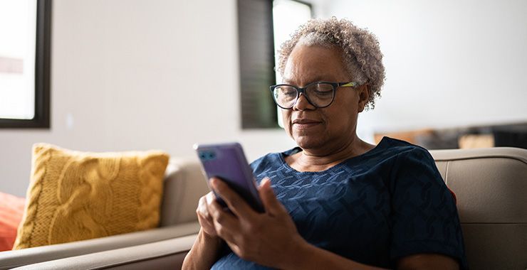 an older woman is sitting on a couch using a cell phone .