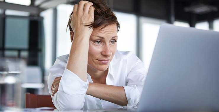 a woman is sitting at a desk looking at a laptop computer .