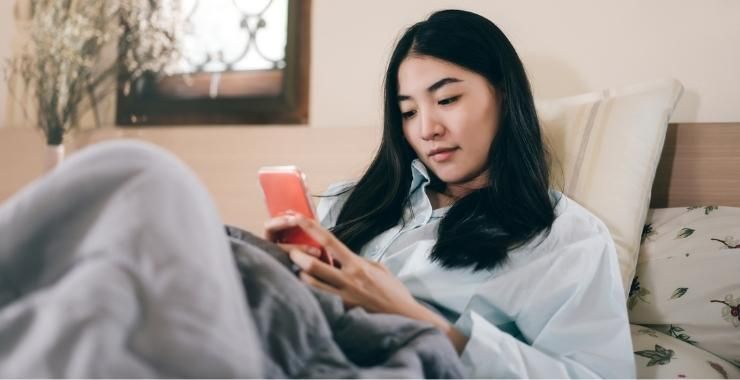 a woman is laying in bed looking at her cell phone .