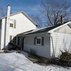 A white house with snow on the ground and a chimney