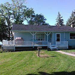 A blue house with a porch and a grill in the backyard.