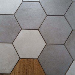 A close up of a hexagon tile floor with a wooden floor in the background.