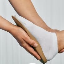 Una persona tiene in mano una soletta ortopedica sagomata di colore beige, premuta contro la pianta del piede di una persona che indossa un calzino bianco.