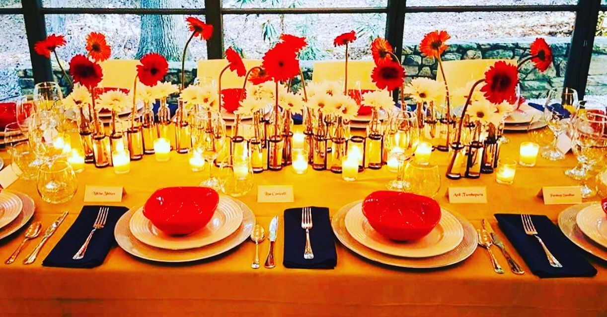 A table with plates , bowls , utensils and flowers on it.