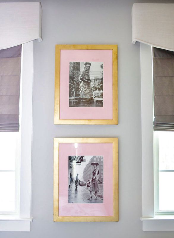 Two framed pictures are hanging on a wall next to two windows