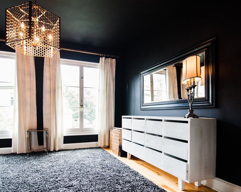 A living room with black walls , a white dresser , a mirror and a chandelier.