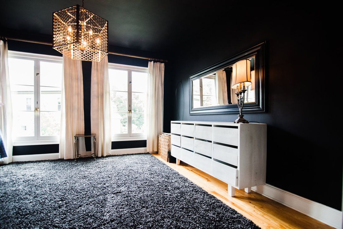 An empty room with black walls , a white dresser , a mirror and a chandelier.