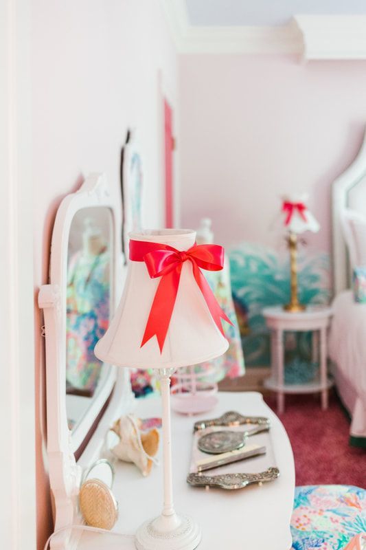 A lamp with a red bow on it is sitting on a dresser in a bedroom.