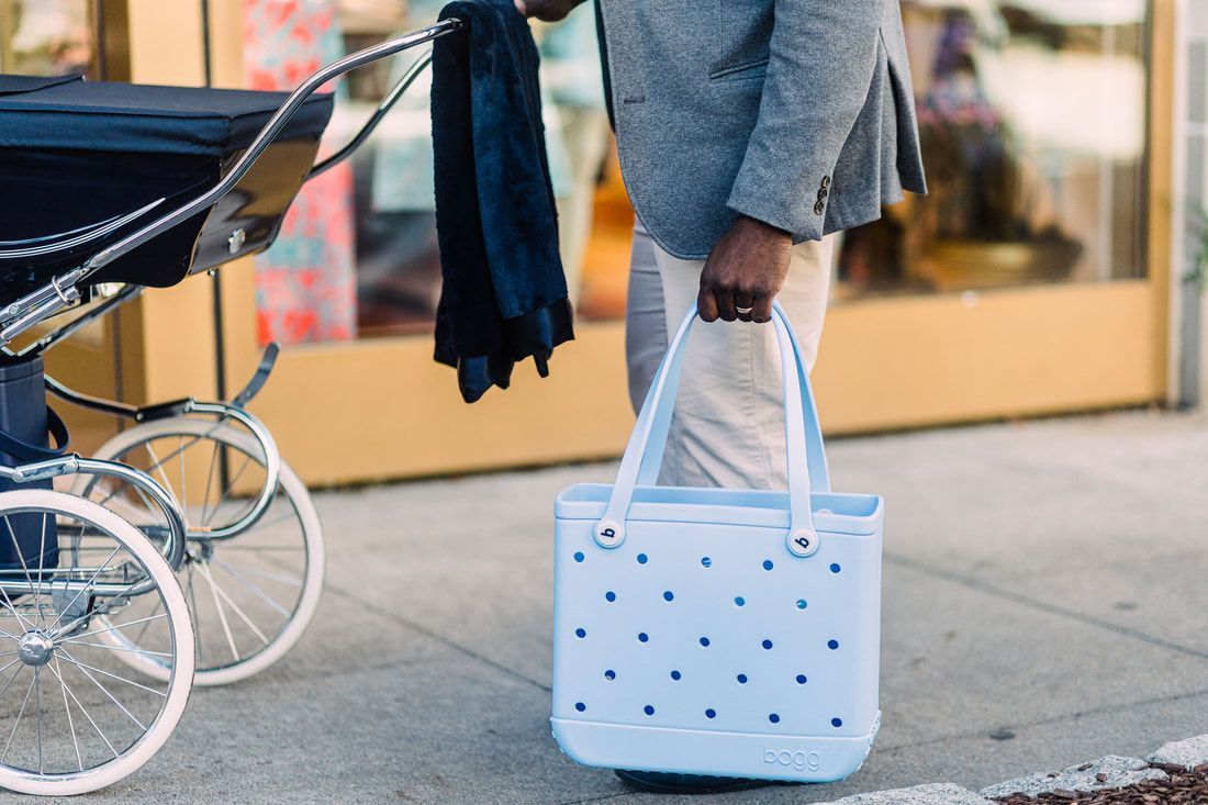 A man is holding a blue tote bag while standing next to a stroller.