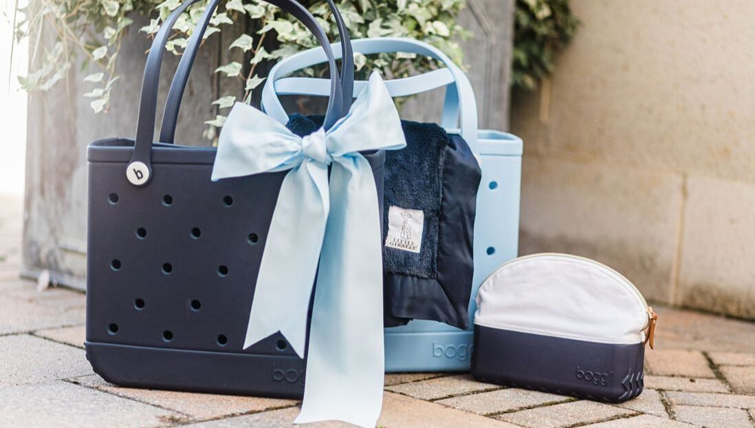 A purse with a bow on it is sitting on a brick sidewalk next to a plant.