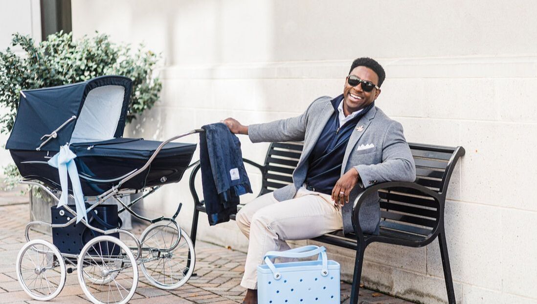 A man is sitting on a bench next to a stroller.