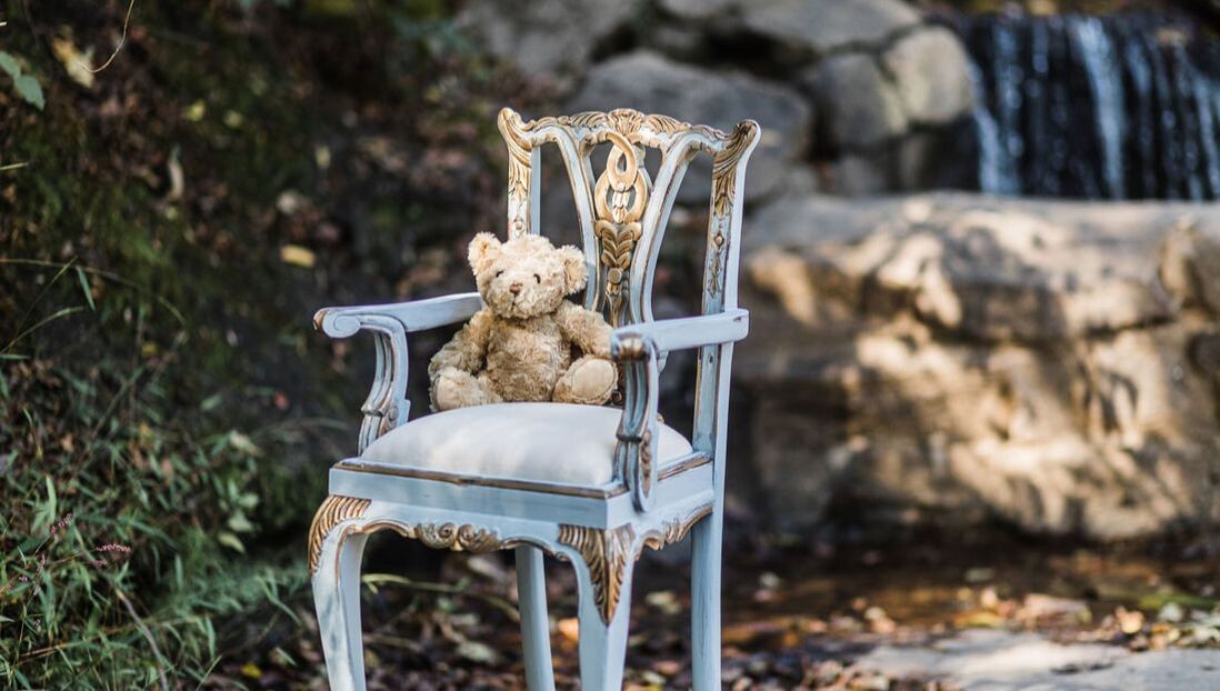 A teddy bear is sitting on a chair in front of a waterfall.