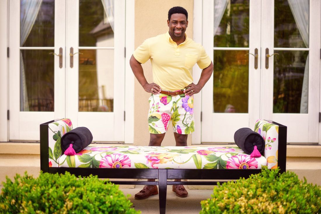 A man in a yellow shirt and floral shorts is standing next to a bench.