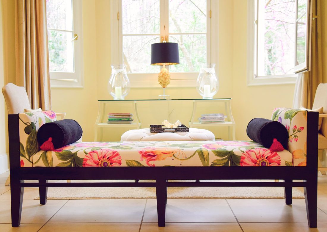 A bench with flowers on it is in a living room next to a window.