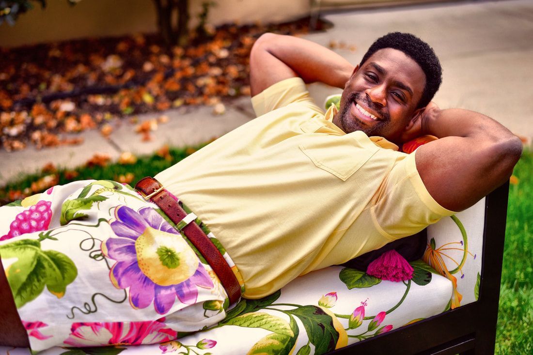 A man is laying on a couch with his hands behind his head.