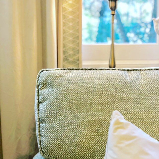 A green couch with a white pillow and a lamp in front of a window.