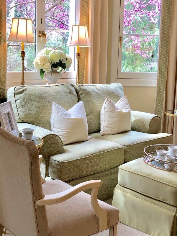 A living room with a couch , chair , ottoman and lamps.