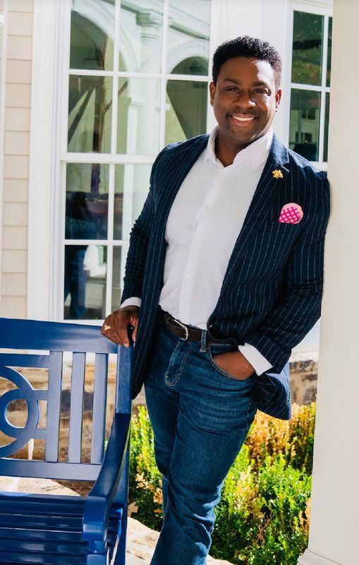 A man in a suit and tie is standing next to a blue bench.