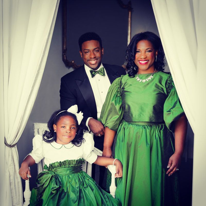 A man in a tuxedo stands next to a woman in a green dress and a little girl in a green dress