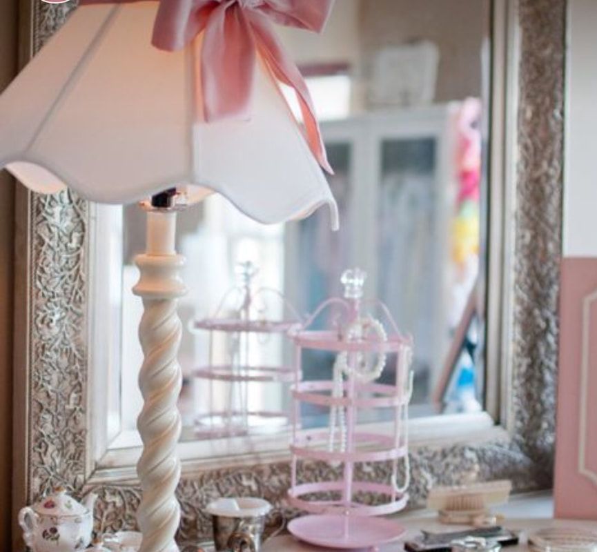 A lamp with a pink bow on it sits in front of a mirror