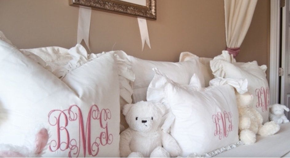 A bed with monogrammed pillows and teddy bears on it
