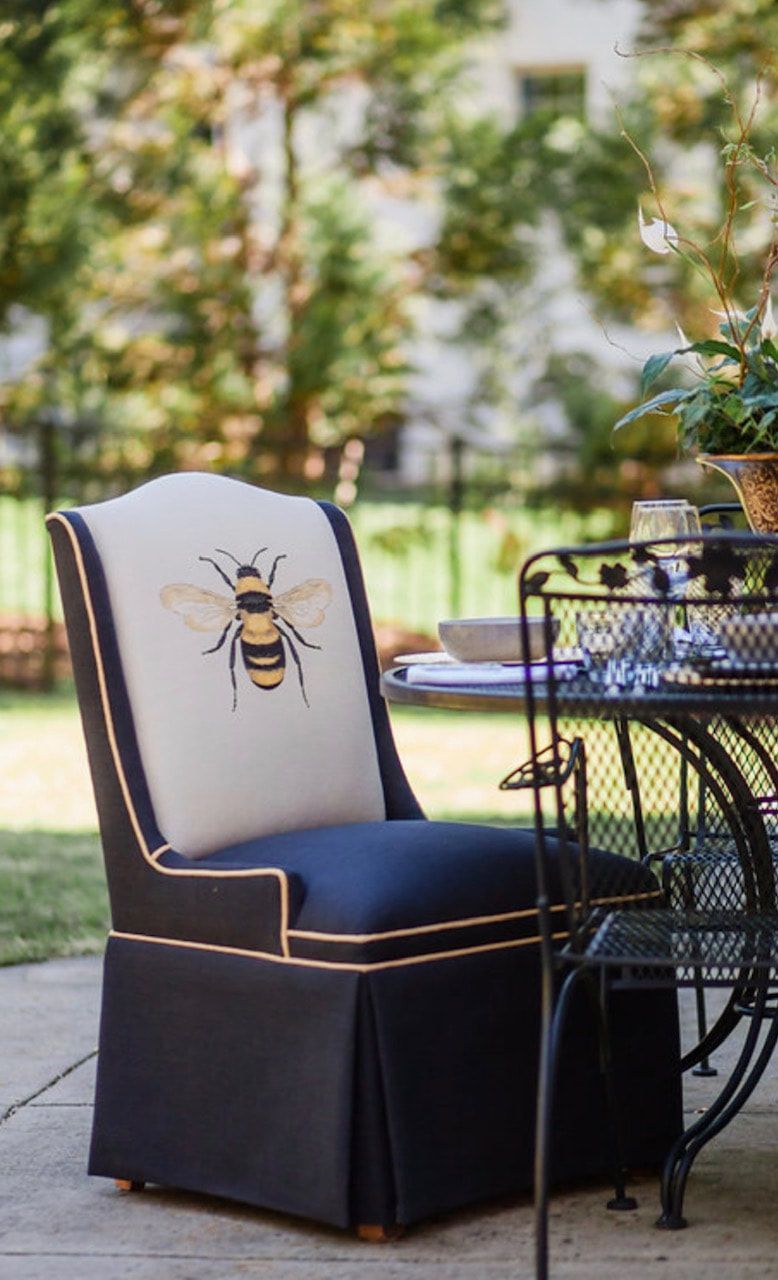 A chair with a bee embroidered on the back is sitting on a patio next to a table.