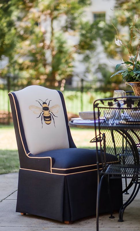 A chair with a bee on it is sitting next to a table on a patio.